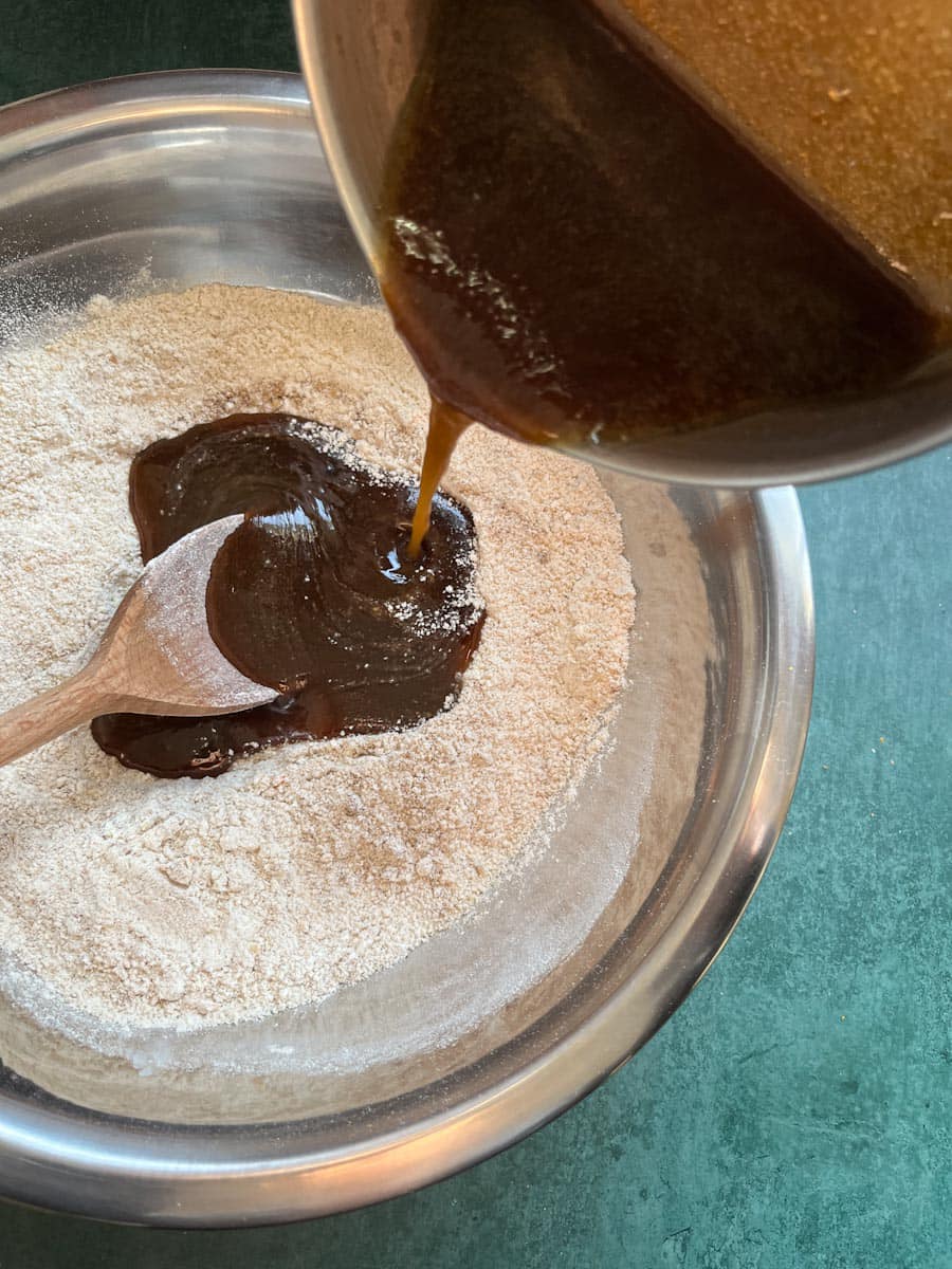 a saucepan of melted brown sugar and butter being poured into a large silver bowl of flour.