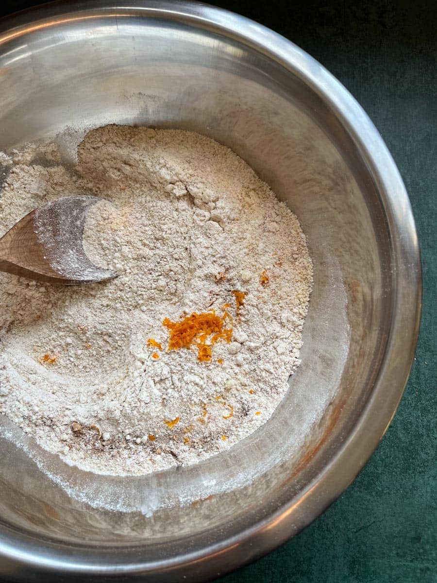 a large silver mixing bowl of flour, spices and grated orange zest.