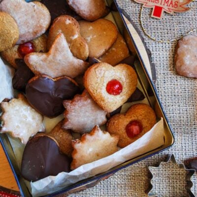 A box filled with German gingerbread cookies glazed with icing sugar, coated in chocolate and topped with glace cherries.