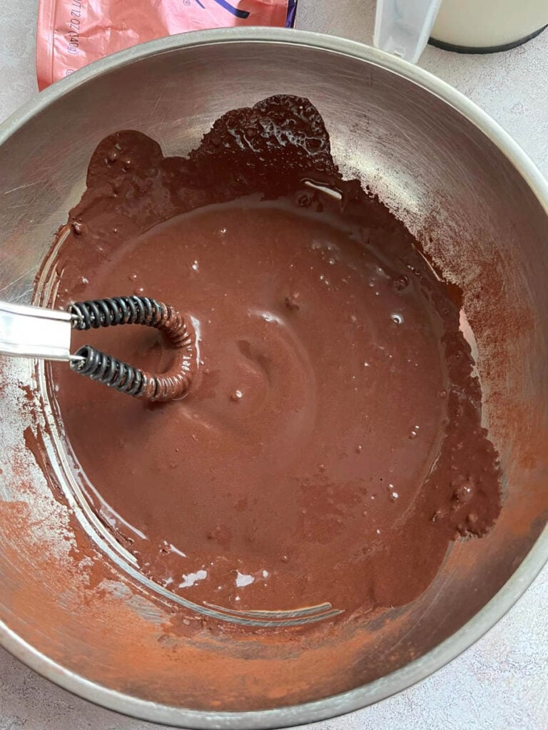 cocoa powder and milk whisked together to make a paste in a silver bowl.
