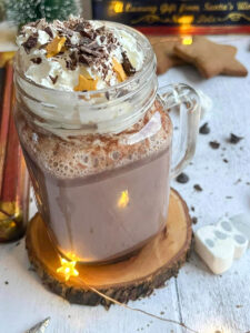 a glass mug of hot chocolate topped with whipped cream, grated chocolate and gold stars.