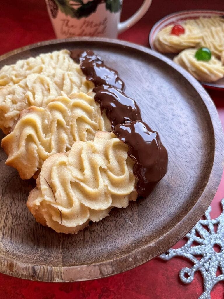 chocolate dipped piped biscuits on a wooden cake stand.
