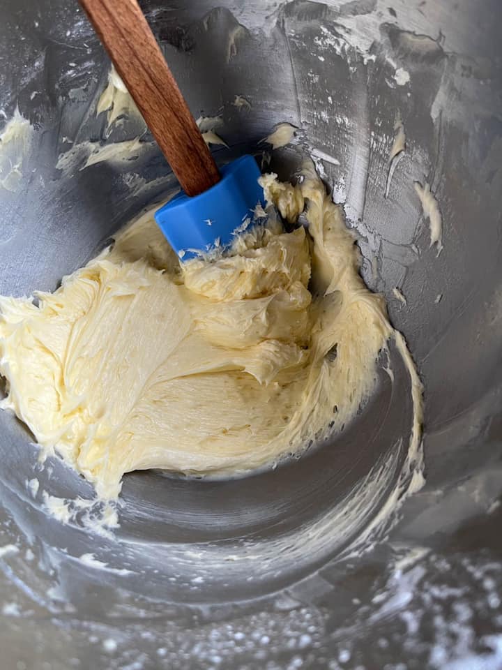 a silver bowl of creamed butter and sugar with a blue wooden handled spatula.