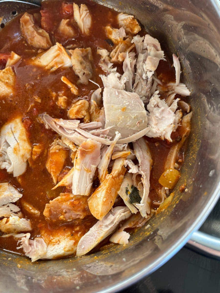 a silver pan of cooked turkey being stirred into a curry sauce.