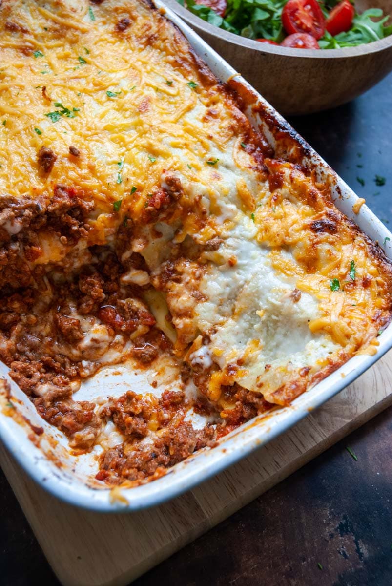 Homemade minced beef lasagne topped with melted cheese in a white dish. 
