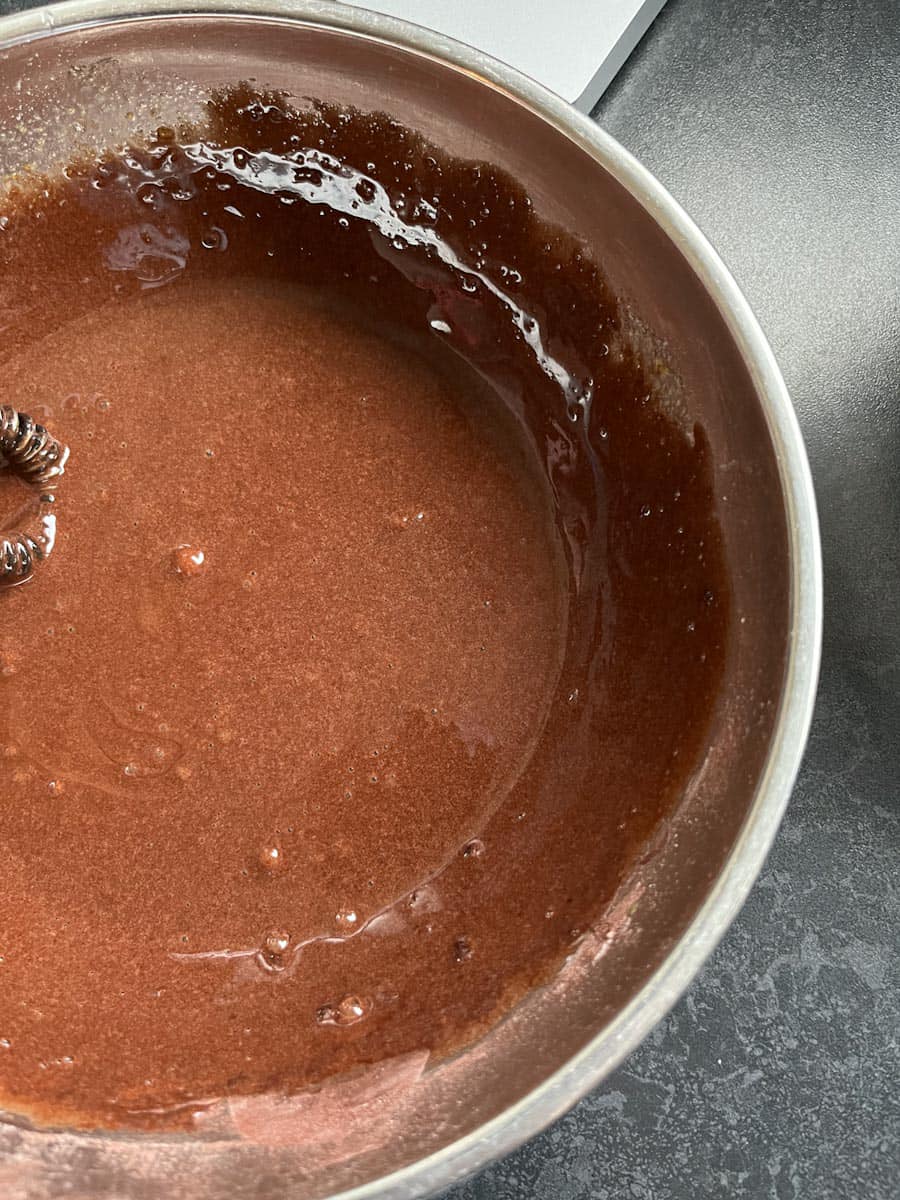 a silver mixing bowl with beaten chocolate, sugar and eggs.