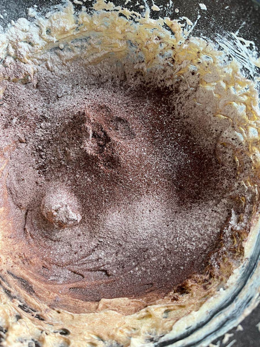 a glass mixing bowl of chocolate powder and flour being stirred into a cake batter.