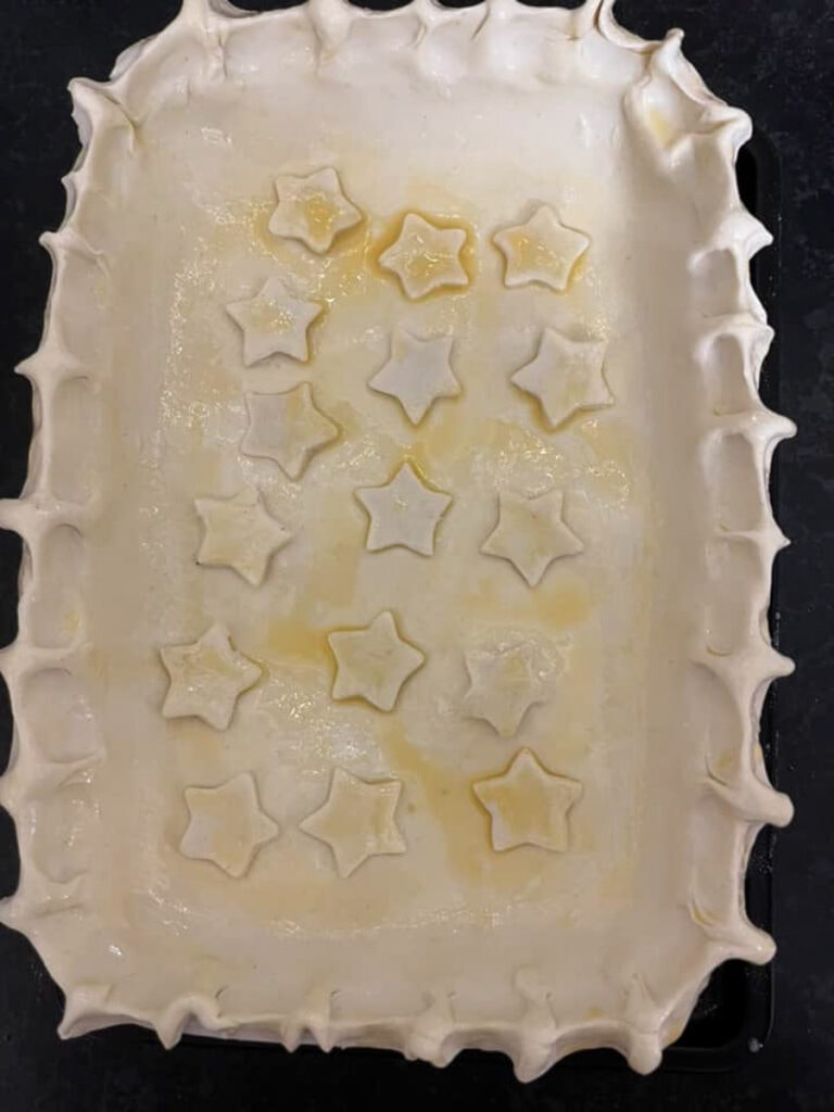 an unbaked steak pie with a crimped puff pastry lid decorated with pastry stars and glazed with egg.