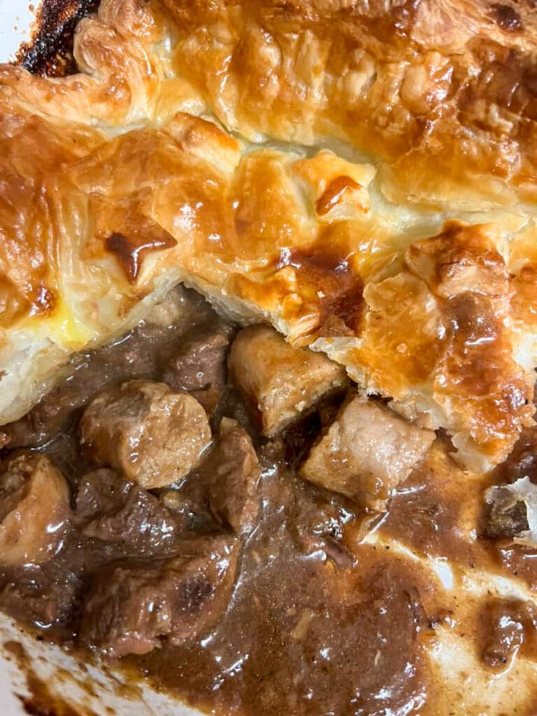 a partially eaten steak and sausage pie with a golden puff pastry lid.