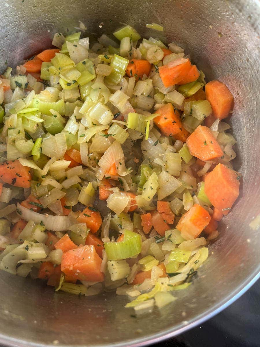 chopped carrot, onion, leek, celery and herbs being gently cooked in a silver pan.