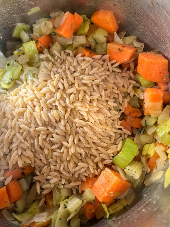 a silver pan of chopped carrots, leek, onion, celery and orzo pasta.