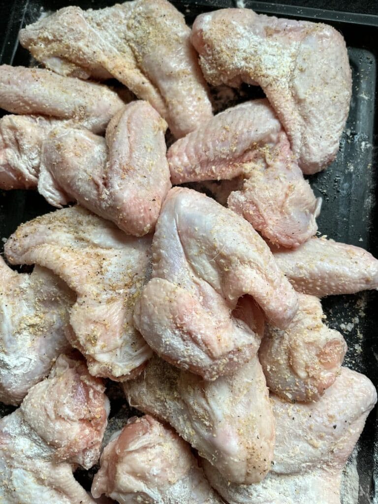 a tray of raw chicken wings seasoned with garlic granules, salt and pepper.