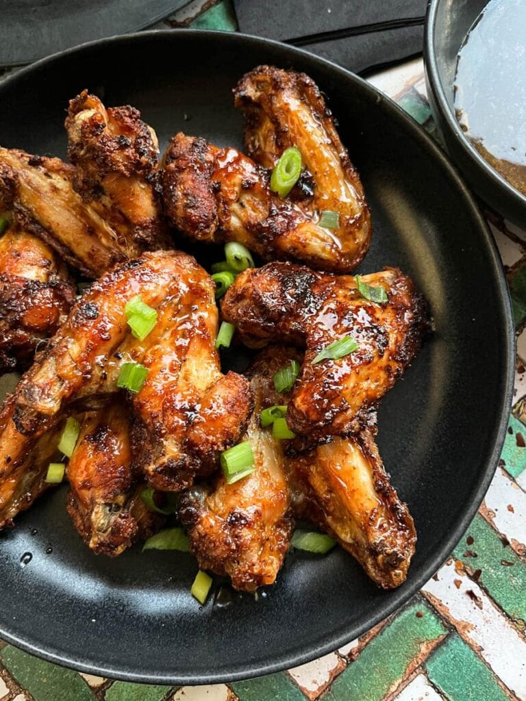 a black bowl of cooked chicken wings sprinkled with chopped green onion.