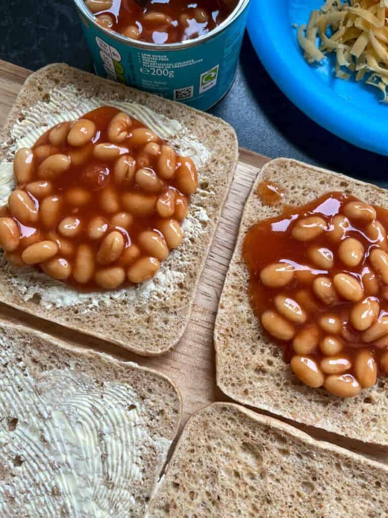 A wooden chopping board with slices of brown bread topped with baked beans.