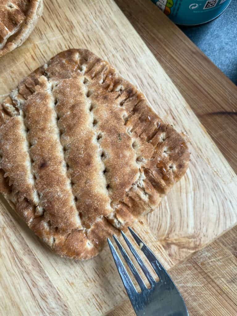 a small brown sandwich on a wooden chopping board and a metal fork.