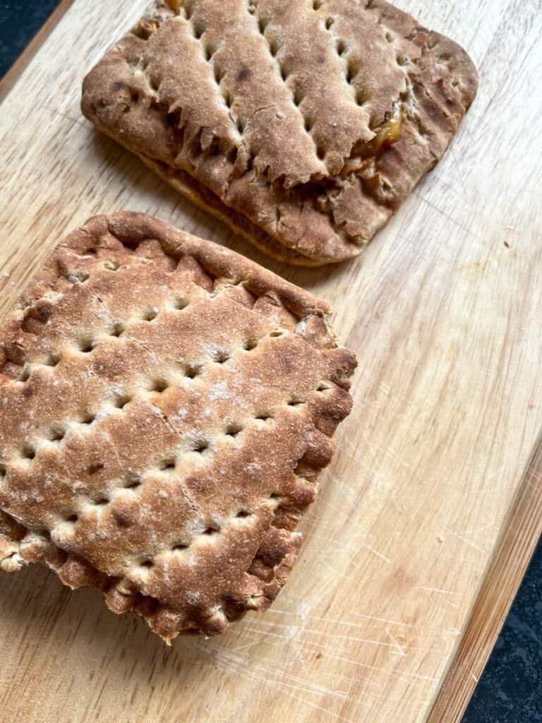 two small brown sandwiches on a wooden chopping board.