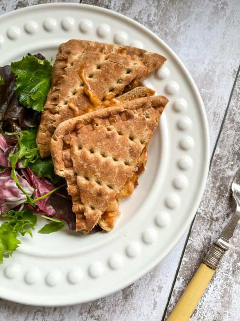 a toasted sandwich filled with melted cheese and baked beans and a side salad on a white plate.