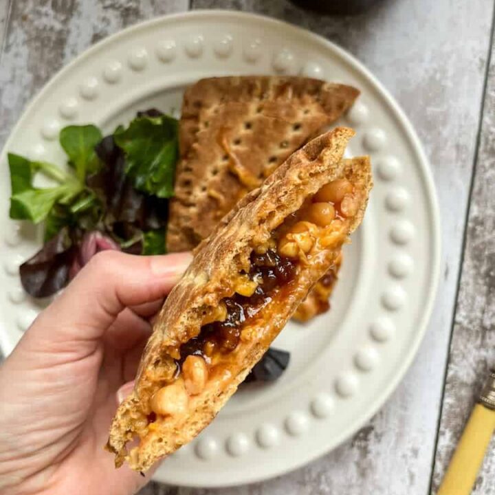 a hand holding a melted cheese, bean and pickle toasted sandwich.