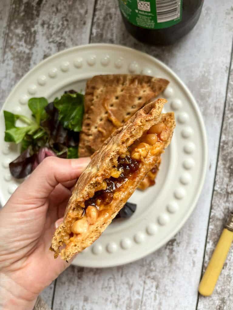 a hand holding a melted cheese, bean and pickle toasted sandwich.