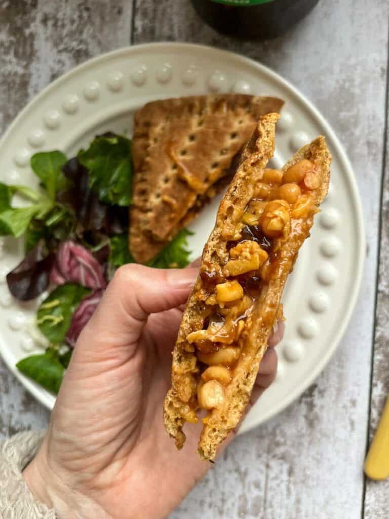 a hand holding a cheese, bean and pickle toasted sandwich.