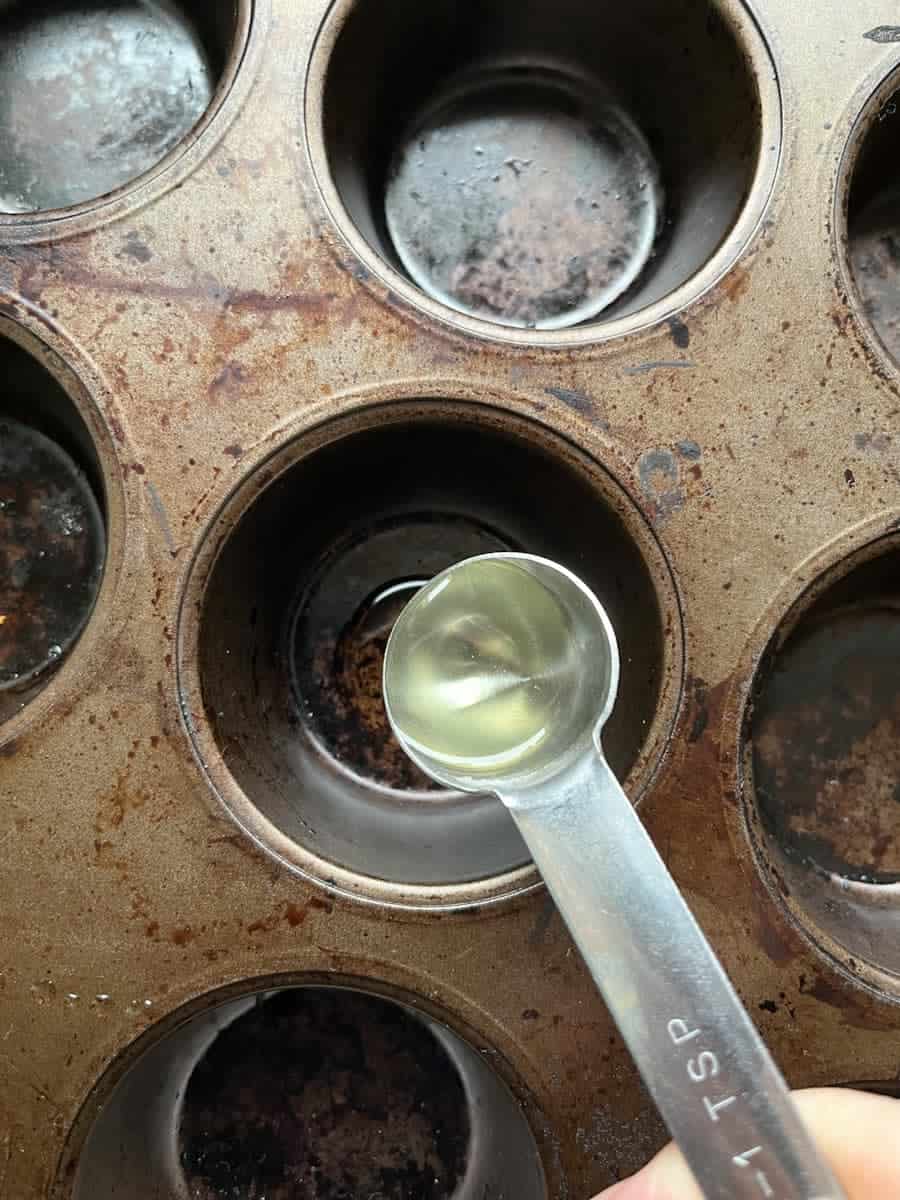 spoonfuls of oil being poured into a muffin tin.
