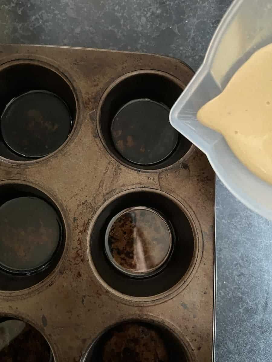 Yorkshire pudding batter being poured from a plastic jug into a muffin tin.