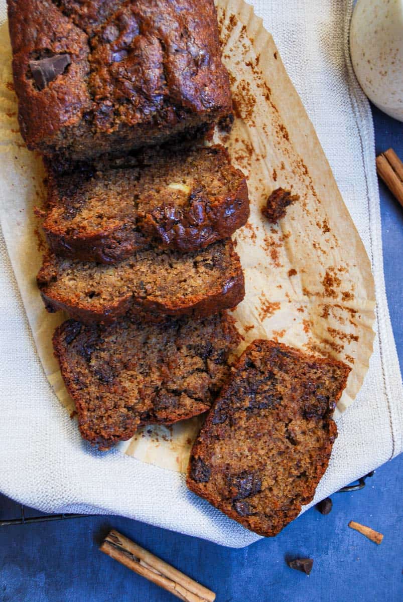 a partially sliced banana bread with chocolate chunks on a wire cooling rack covered with a beige tea towel.