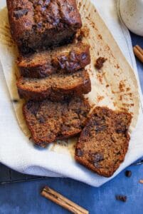 sliced banana bread with chocolate chunks on a wire rack covered with a beige tea towel.