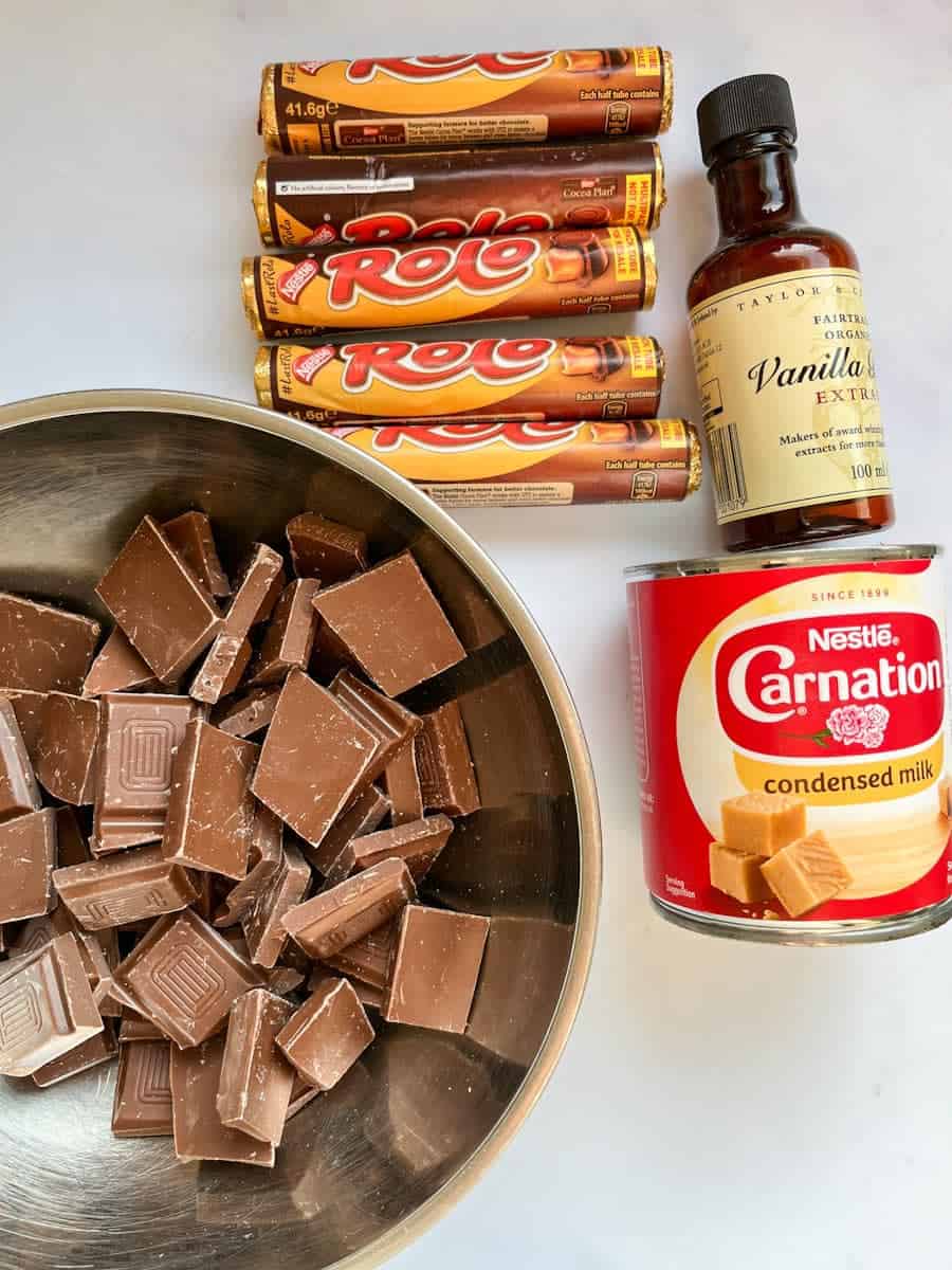 A silver bowl of chopped milk chocolate, a tin of Nestle condensed milk, a bottle of vanilla extract and five packets of Rolo sweets.