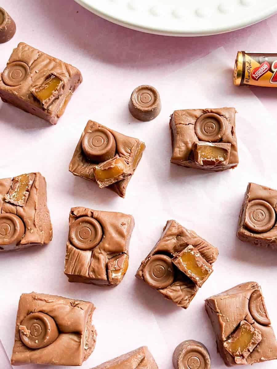 Squares of chocolate fudge topped with Rolos on a piece of baking parchment.