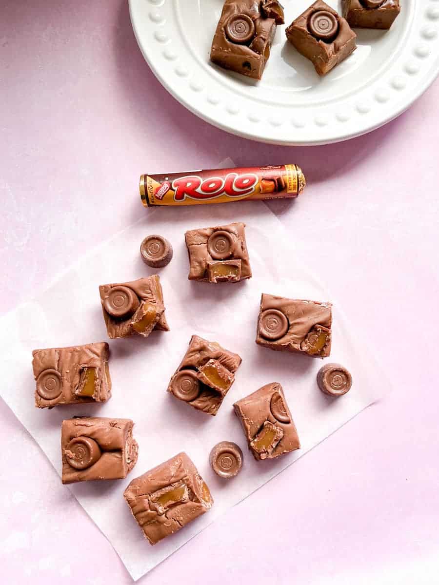 square of chocolate fudge topped with Rolos on a piece of baking parchment, a packet of Rolo sweets and a white plate of chocolate Rolo fudge.