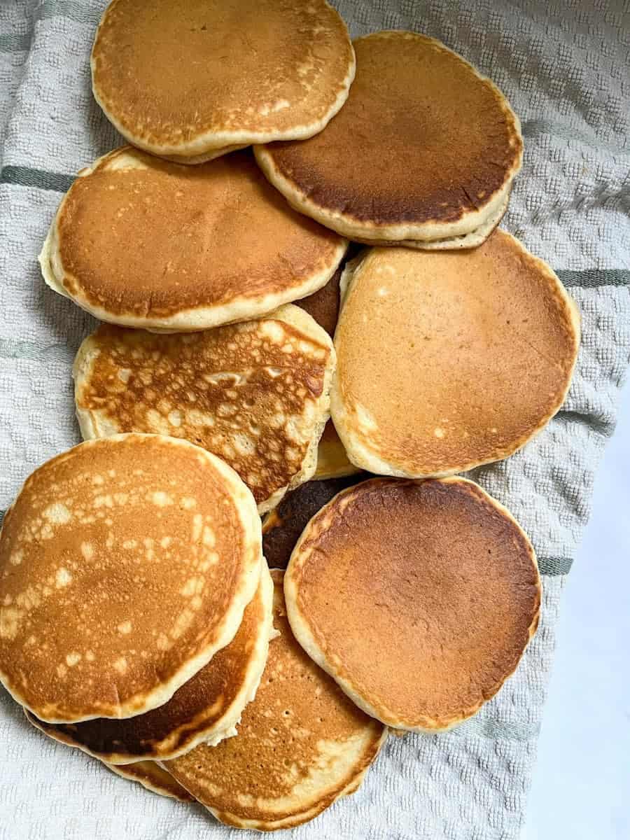 a batch of freshly made golden pancakes on a white and grey tea towel.