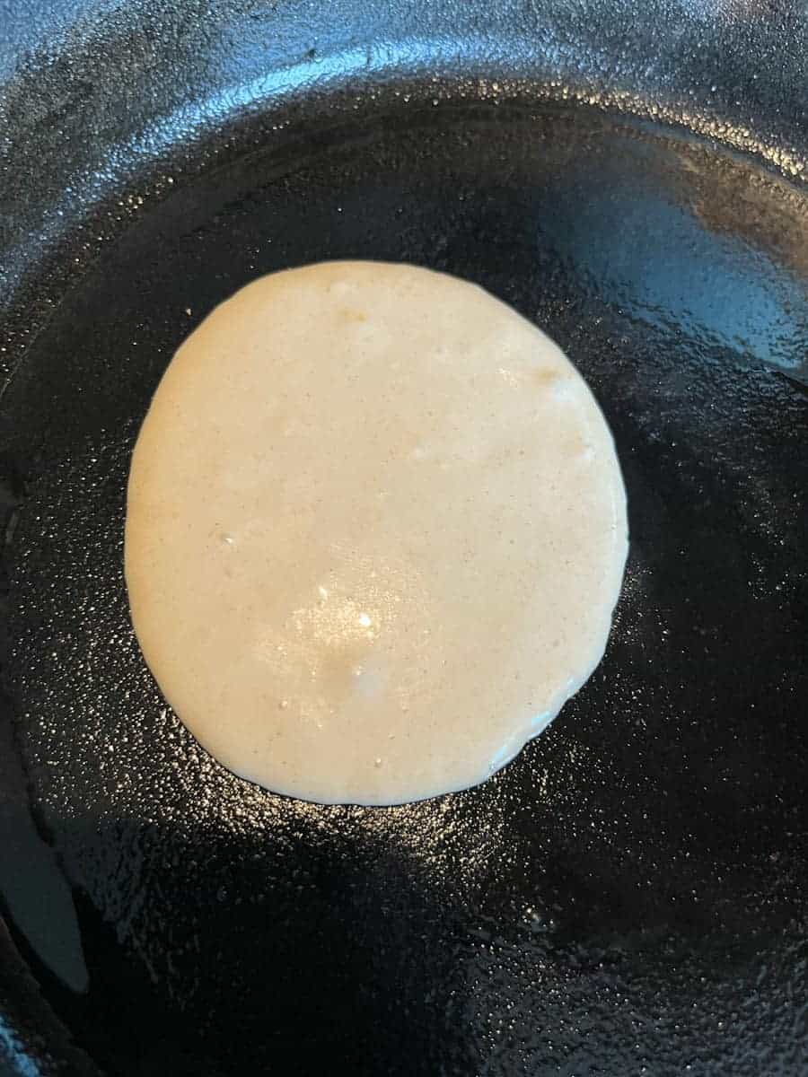 a round pancake being cooked in a cast iron pan.