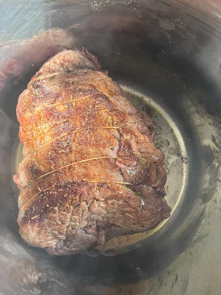 a piece of brisket beef browning in a silver pot.