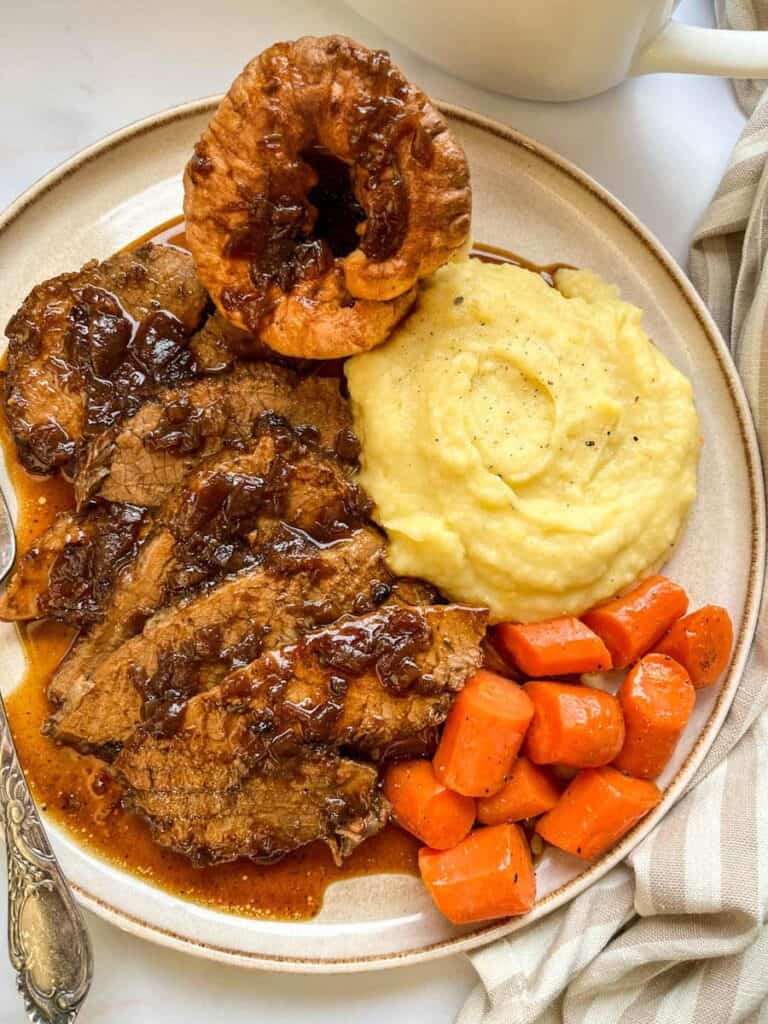 a plate of beef slices in onion gravy with mashed potatoes and carrots. 