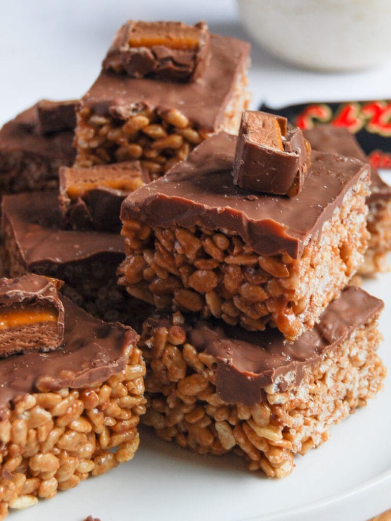 Mars bar crispy squares topped with milk chocolate on a white plate.