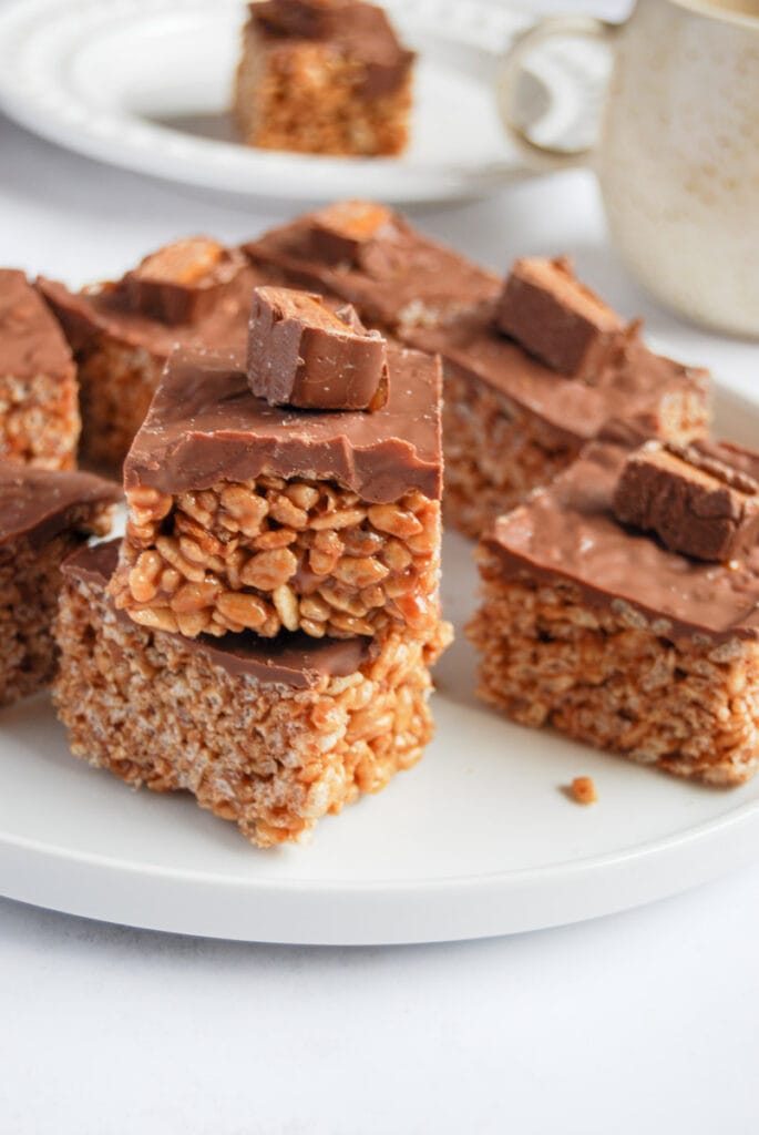 a white plate of chocolate Mars bar crispy slices and a beige mug.