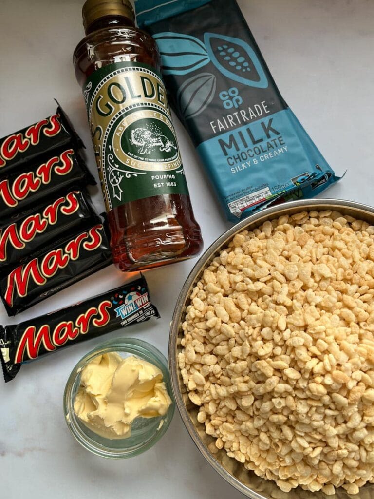 a silver bowl of rice crispies, a small dish of butter, a tub of golden syrup, five Mars Bars and two packets of milk chocolate.