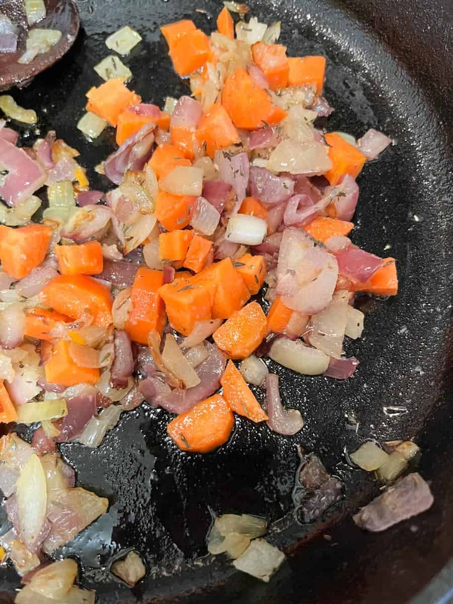 chopped onions and carrots cooking in a cast iron pan.