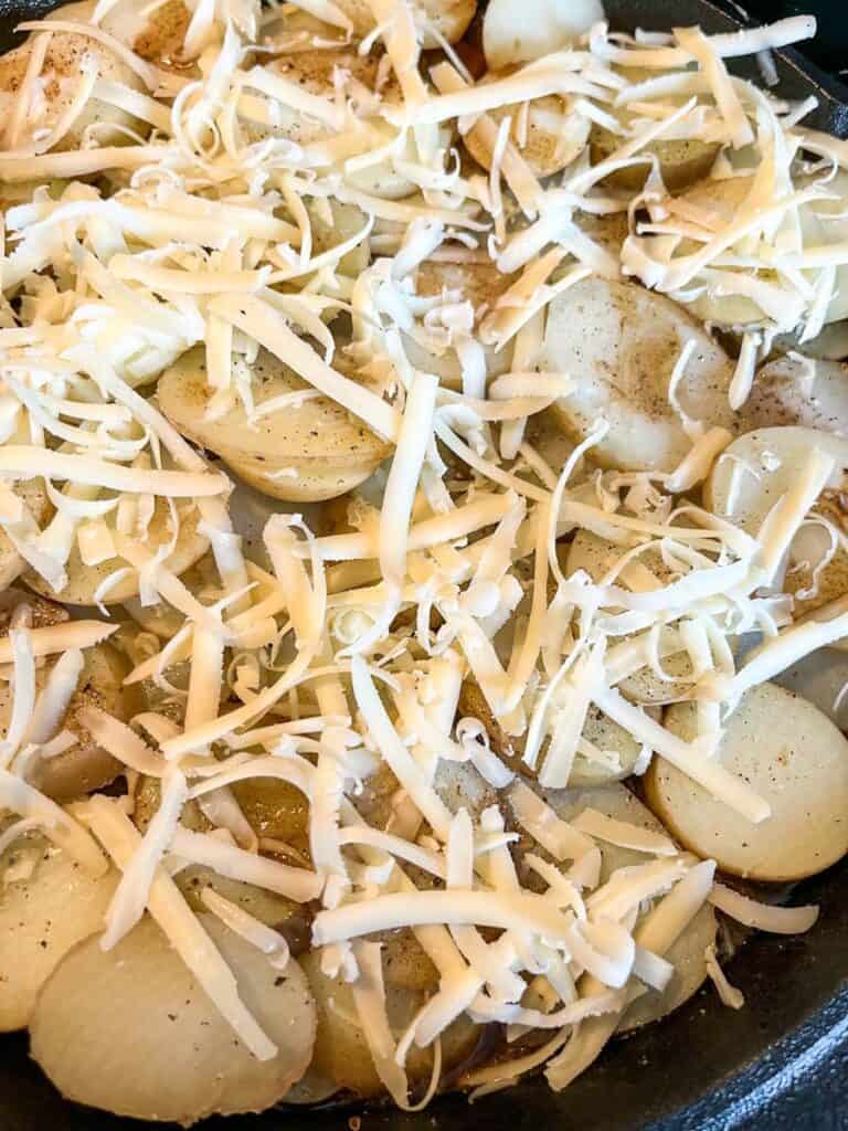 grated cheese on top of sliced potatoes in a round cast iron pan.