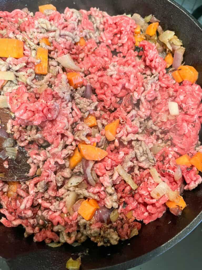 minced beef browning in a pan with onions and carrots.
