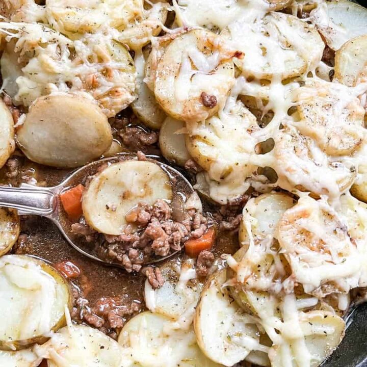 a pan of minced beef and carrots in gravy topped with sliced potatoes and grated cheese.