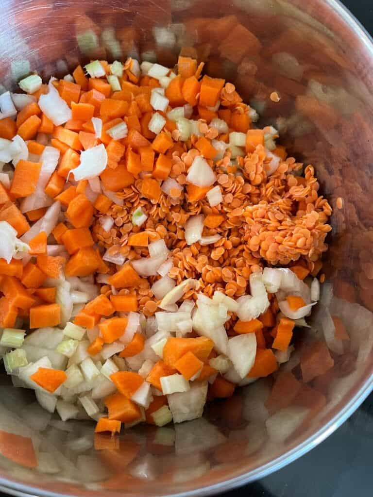 a silver bowl of red lentils, diced onion, celery and carrot.