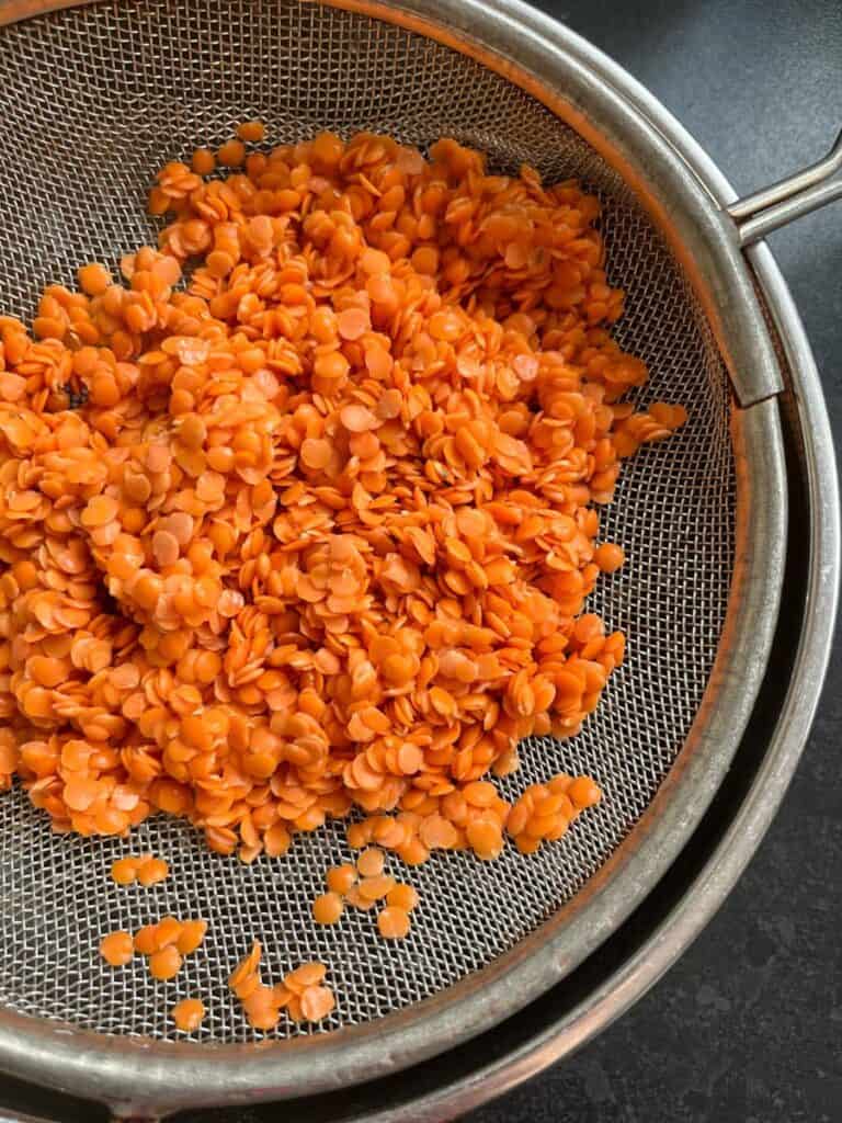 Red split lentils in a metal sieve.