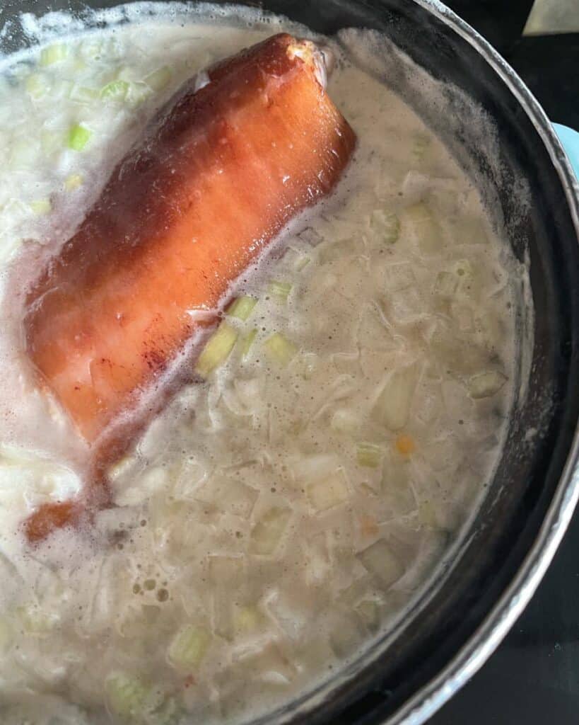 A ham hock simmering in a large pan of water with diced onion, celery and carrot.