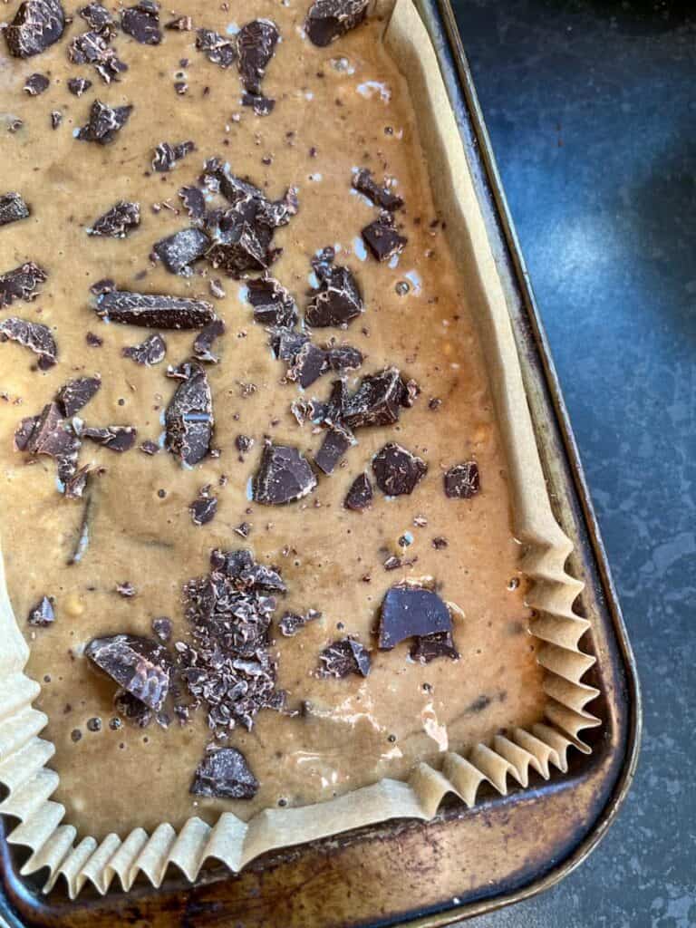 banana bread batter with dark chocolate chunks scattered on top in a lined loaf tin.