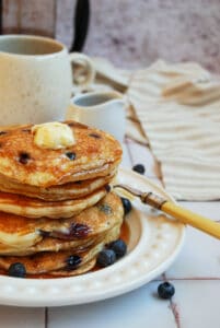 a stack of blueberry pancakes with butter and maple syrup on a white plate.