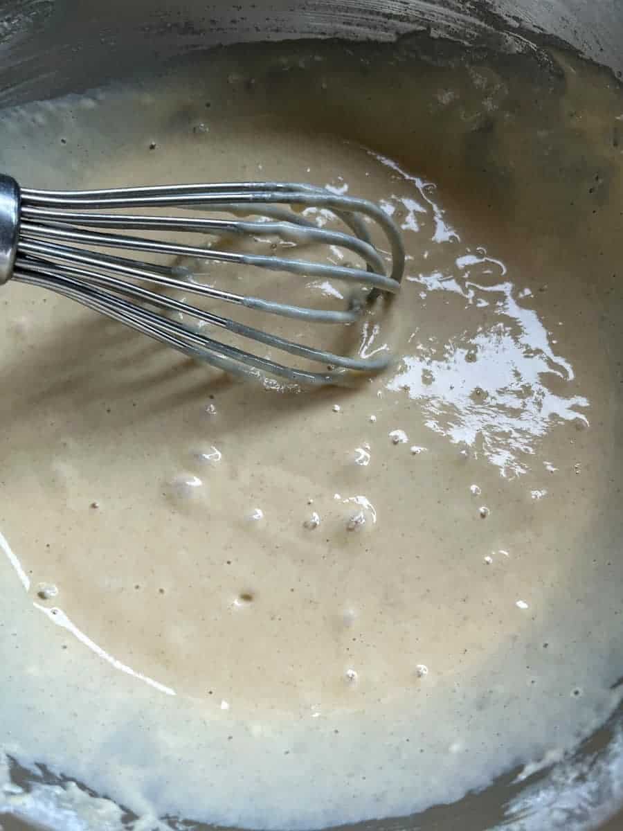 a large silver mixing bowl of buttermilk pancake batter with a metal whisk.