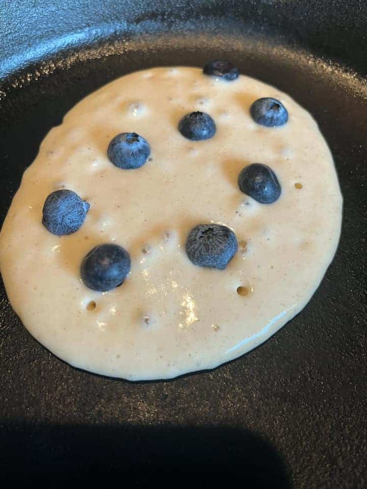 a blueberry pancake cooking in a frying pan.