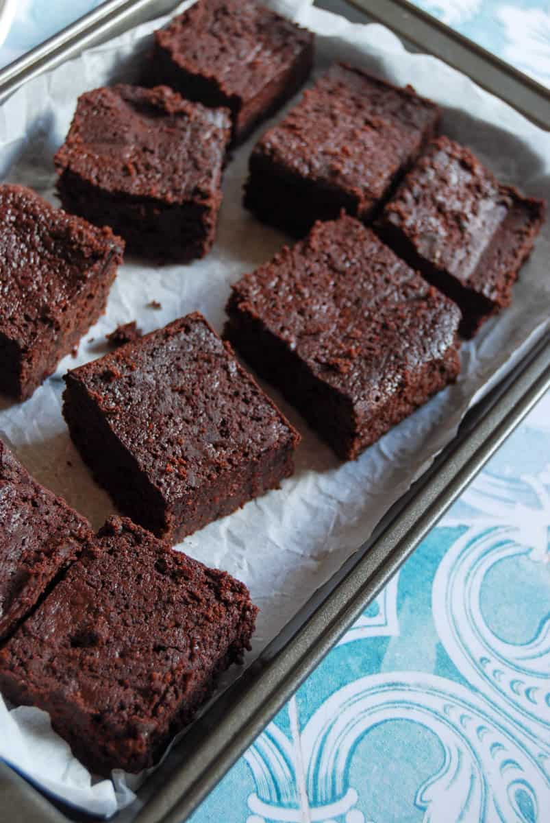 chocolate brownies in a lined baking tin on blue and white patterned tiles.